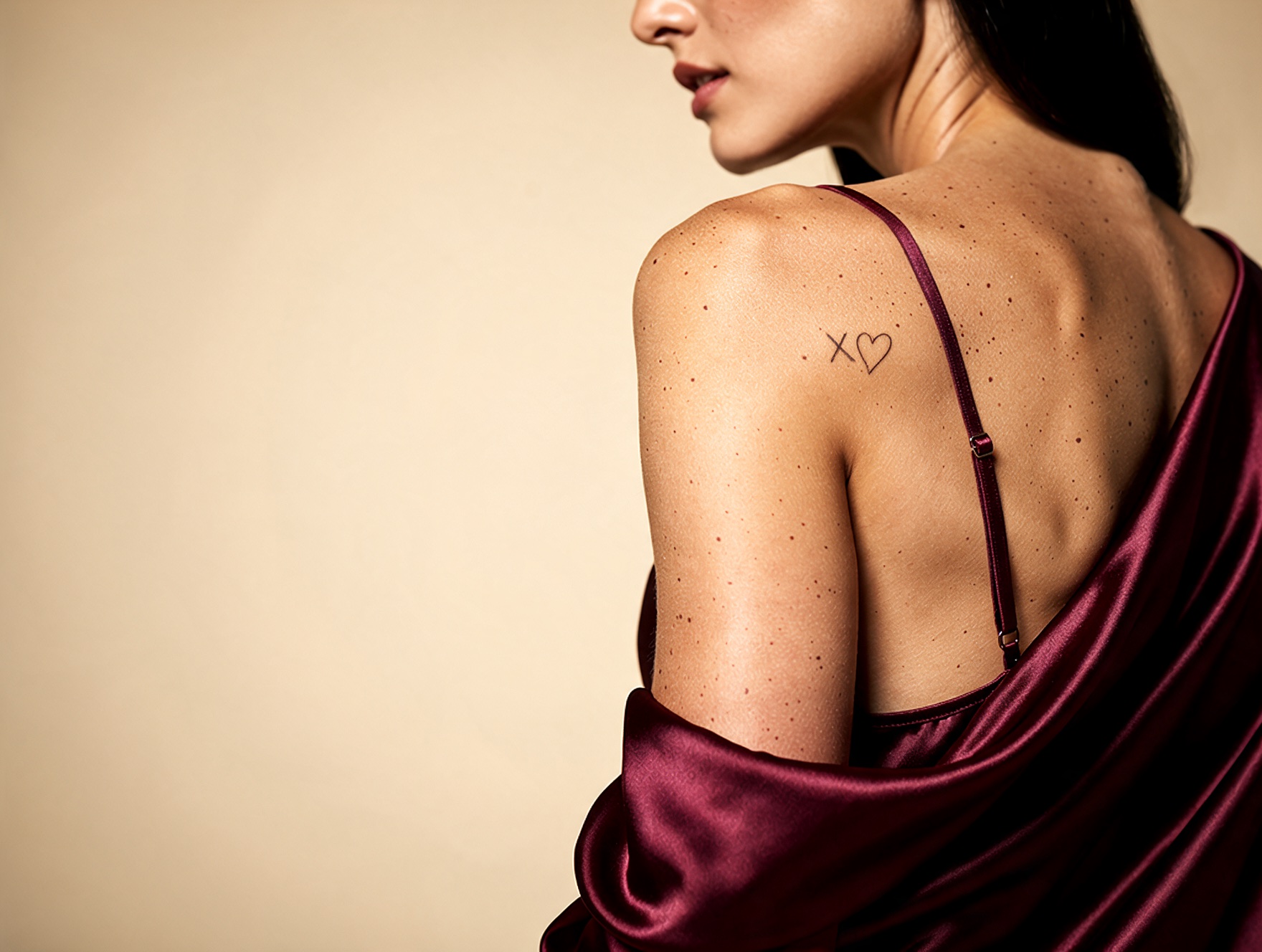 A woman's bare back draped in flowing burgundy satin against a warm champagne backdrop