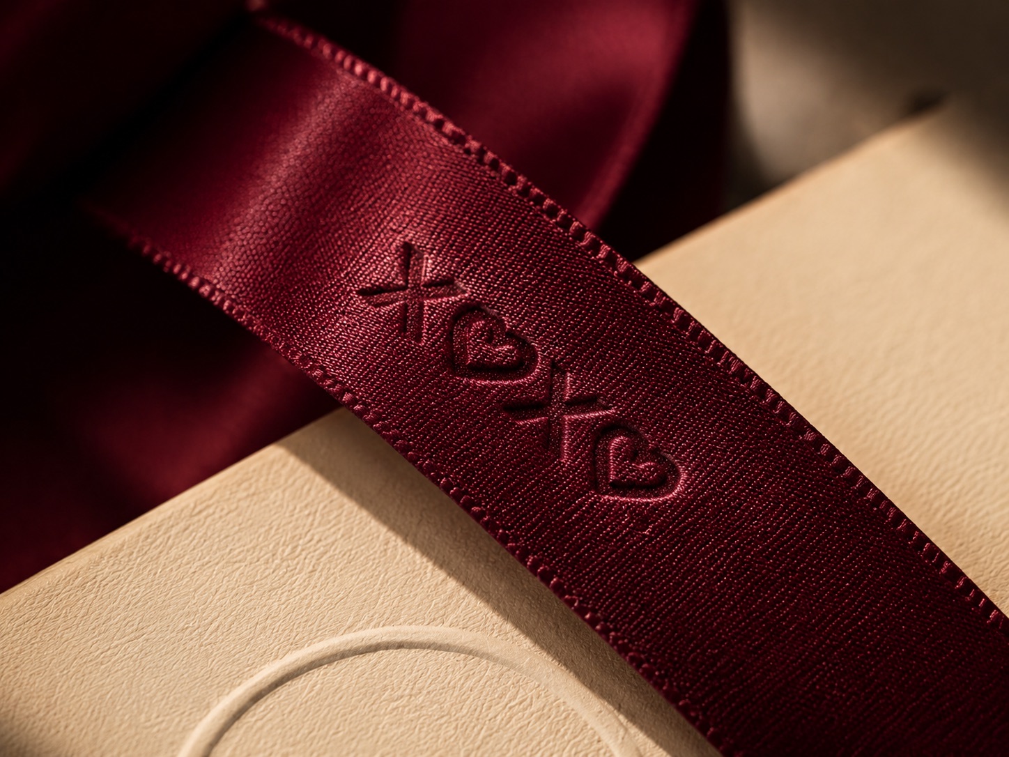Burgundy satin ribbon embossed with the XOXO logo resting on a cream box